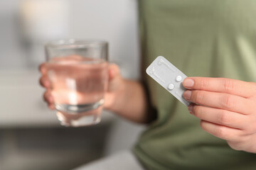Woman taking emergency contraception pill in bedroom, focus on hand