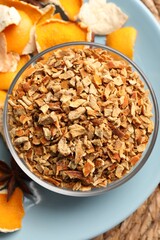 Bowl of dried orange zest seasoning, fresh peel and anise on wicker mat, flat lay