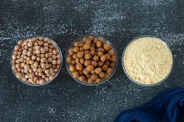 Cooked and raw chickpeas and chickpea flour in three bowls on dark background. Top table view. A closeup. Protein gluten-free food, healthy vegetable, garbanzo bean legume concept.