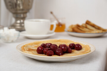 Pancakes with cherries, vintage samovar and cup of hot drink served on table. Traditional Russian tea ceremony