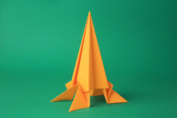 Origami art. Handmade yellow paper rocket on green background