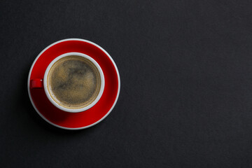 Red ceramic cup with hot aromatic coffee on black background, top view. Space for text