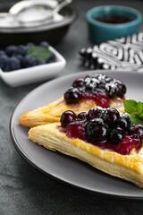 Fresh tasty puff pastry with sugar powder, jam, sweet berries and mint on grey table, closeup