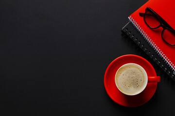 Red cup with aromatic cappuccino, notepads and glasses on black background, flat lay. Space for text