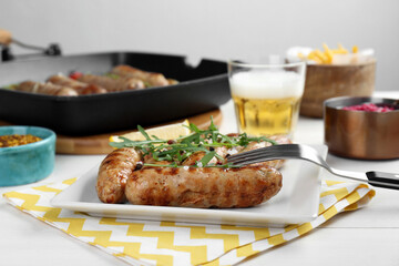 Tasty grilled sausages served with arugula and beer on white wooden table, closeup