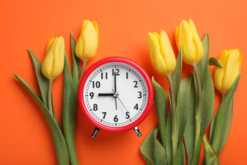 Red alarm clock and beautiful tulips on orange background, flat lay. Spring time