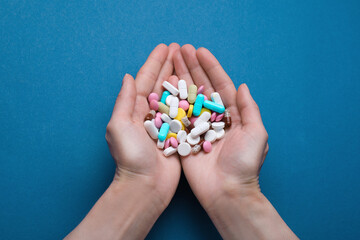 Woman holding colorful antidepressants on blue background, top view