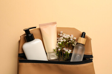 Preparation for spa. Compact toiletry bag with different cosmetic products and flowers on beige background, top view