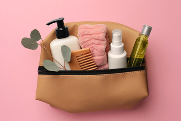 Preparation for spa. Compact toiletry bag with different cosmetic products and eucalyptus on pink...