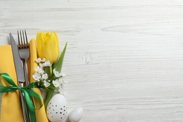 Cutlery set, Easter eggs and beautiful flowers on white wooden table, flat lay. Space for text