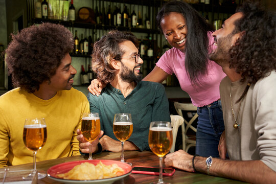 Multiracial group photo of smiling friends gathered at restaurant bar after work at pub happy hour. Cheerful colleagues having fun together drinking alcohol indoors. People enjoying the leisure.