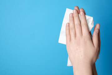 Woman wiping hands with paper towel on light blue background, closeup. Space for text