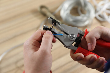 Professional electrician stripping wiring at wooden table, above view