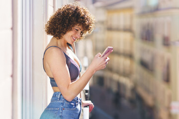 Cheerful woman using smartphone on balcony