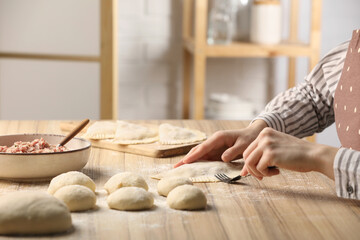 Woman making chebureki at wooden table indoors, closeup