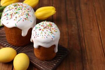 Tasty Easter cakes, decorated eggs and flowers on wooden table. Space for text