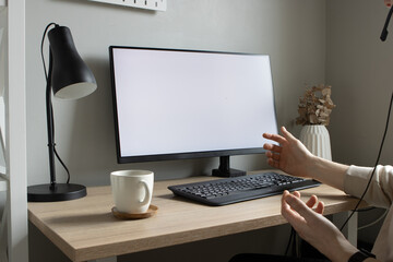Person in a meeting, working from home on laptop with larger monitor in the background and witha a coffee mug in the foreground.