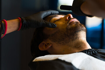 Caucasian relaxed man shaving his beard at the barber shop