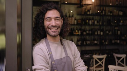 Close up video young adult local small business owner looking at camera. Happy male bartender with positive attitude. Cheerful worker smiles while standing leaning on bar door. Confident people. - Powered by Adobe