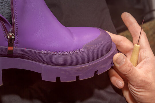 Shoemaker examines the seam on the boot made with an awl and thread. Shoe repair. Close-up
