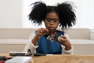Smiling child girl student learning and building project toy robotics technology at home. Girl student training and control toy robot in classroom at school