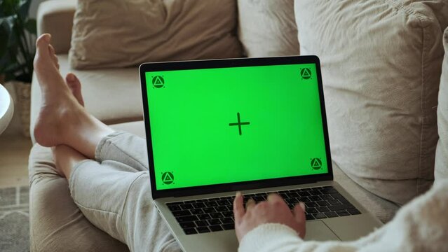 Woman using laptop green screen chroma key, typing and working, lying on sofa at home, camera zoom