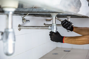 Technician plumber using a wrench to repair a water pipe under the sink. Concept of maintenance,...