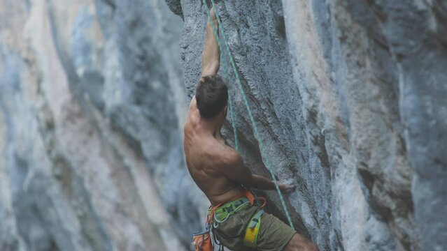 A strong man climbs a rock. Strong muscles. Endurance and strength training, man in extreme sport, Rock climber trains in nature.