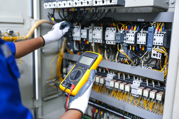 Electricity or electrical maintenance service, Electrician hand holding measuring meter checking electric current voltage circuit breaker cable wiring check main power load center distribution board.