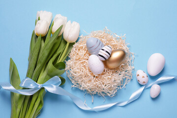 Fototapeta premium Many painted Easter eggs, tulip flowers and ribbon on light blue background, flat lay