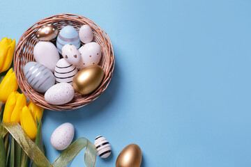 Many painted Easter eggs, tulip flowers and ribbon on light blue background, flat lay. Space for text
