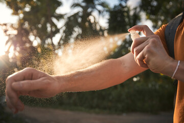 Man is applying insect repellent on his hand against palm trees. Prevention against mosquito bite in tropical destination. .. - 575606491