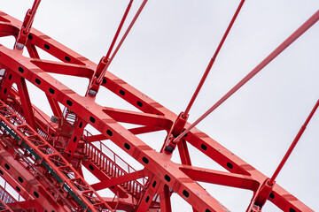 Close-up of fragment of red cable-stayed bridge pylon in place where metal cables are fastened. Close-up shows connection of steel powerful straight crossbar, bridge connection, metal architecture.