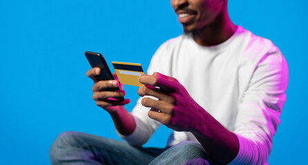Fototapeta premium Unrecognizable black guy holding smartphone and credit card, cropped