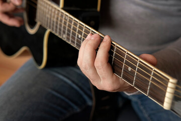 Playing the guitar. Strumming black acoustic guitar. Musician plays music. Man fingers holding mediator. Male hand playing guitar neck in dark room. Unrecognizable person rehearsing, fretboard closeup
