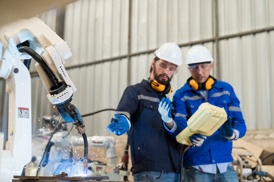 Group of male engineer workers discuss and control robot arm welding at production line plant factory. Engineer workers working automatic robot arm system welding in the smart factory industrial