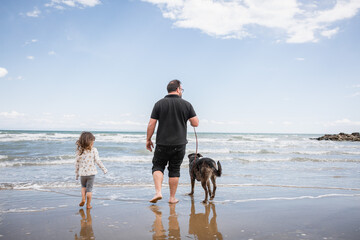 family father, daughter and dog strolling on sand beach