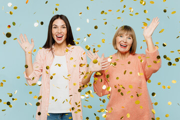 Elder smiling cheerful fun happy satisfied parent mom with young adult daughter two women together wearing casual clothes throw up confetti isolated on plain blue cyan background. Family day concept.