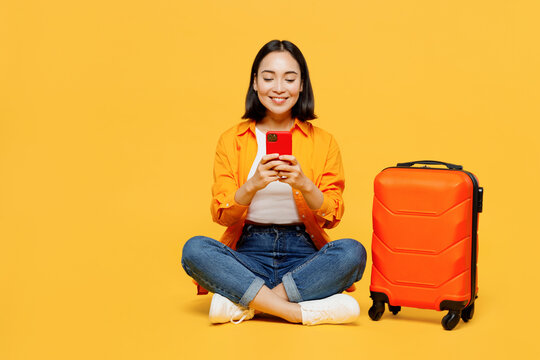 Young woman wear summer casual clothes sit suitcase use mobile cell phone isolated on plain yellow background. Tourist travel abroad in free spare time rest getaway. Air flight trip journey concept.