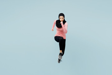Fototapeta na wymiar Full body young asian muslim fitness trainer sporty woman wear pink abaya hijab spend time in home gym running fast jump high isolated on plain blue background studio. Workout sport fit abs concept.