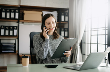 Business asian woman Talking on the phone and using a laptop with a smile while sitting at office.