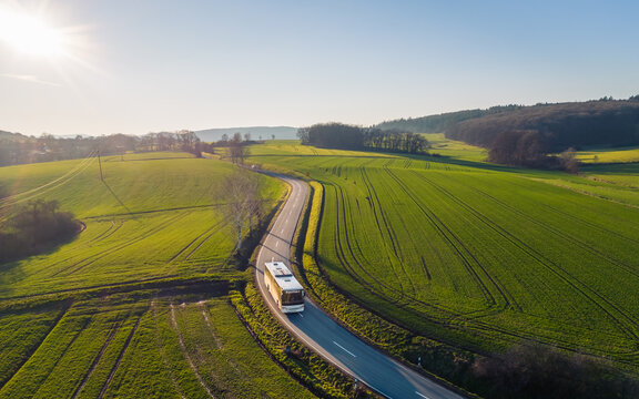 high angle view of bus driving on the winding road through the fields in the countryside under the blue sky
