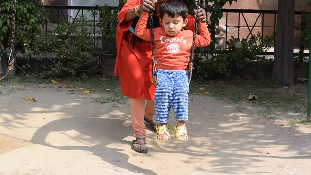 Cute indian boy enjoying swing ride. He is being assisted by his nanny