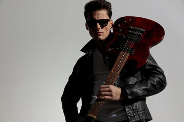 handsome cool man wearing leather jacket and holding guitar on shoulder