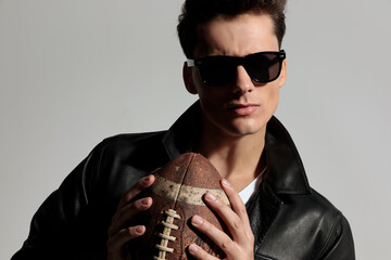 portrait of sexy cool man in leather jacket holding american football ball