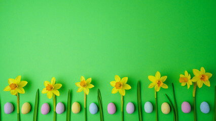 A cheerful spring flat lay display featuring bright yellow daffodils and pastel-colored Easter eggs on a vibrant green background. Banner with copy space