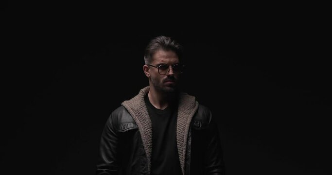 proud cool guy with leather jacket and wool cardigan holding hand in pocket, looking to side and fixing outfit while posing with flash lights on