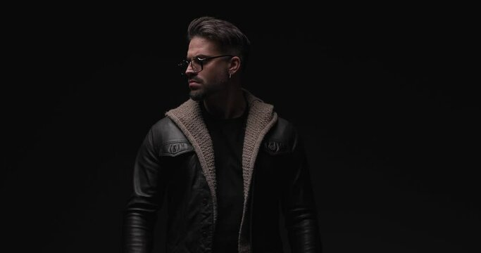 confident casual man looking to side while adjusting leather jacket and wool cardigan, holding hand in pocket and sensually touching lips 