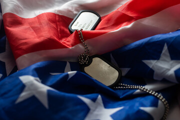 Closeup of a dog tag with the text thank you veterans engraved in it, next to a flag of the United...