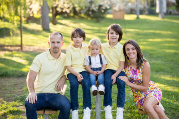 Fototapeta premium Beautiful family, mother, father and three kids, boys, having familly outdoors portrait taken on a sunny spring evening, beautiful blooming garden, sunset time